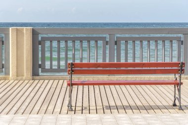 Deniz kenarında bir bank var. Tahta kaldırımda boş basit bir bank. Turistlerin dinlenip yürüyebileceği bir yer. Rıhtım boyunca raylar.