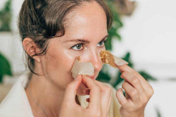 Portrait of a young attractive woman removing gold patches from her face.Self-care at home.Beauty concept.Home interior.Selective focus, close-up.