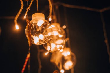 Karanlık bir arka planda yanan ampullerle dolu güzel, yaratıcı bir cam toplar çelengi. Noel ve yeni yıl arkaplanı. Sığ alan derinliğine sahip seçici odak, boşluğu kopyala.