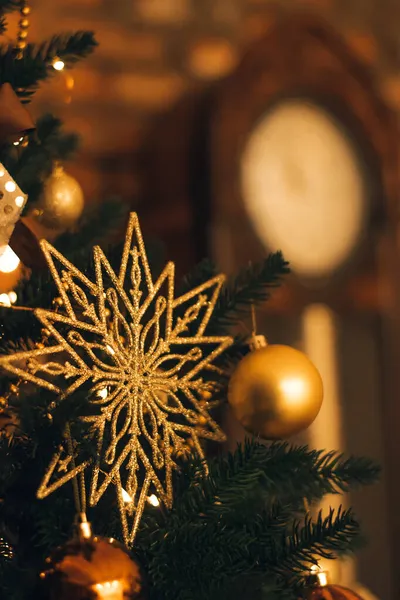 Festive golden decorations of the black Christmas tree in close-up. Blurred large grandfather clock in the dark background.New Year\'s background.Selective focus with shallow depth of field,copy space.