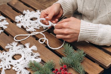 Bir kadın makrome tarzında beyaz pamuktan kar taneleri dokuyor, eko tarzı ev yapımı Noel dekoru, yakın plan eller. Noel, Yeni Yıl ve çevre dostu kavram. Seçici odaklanma.