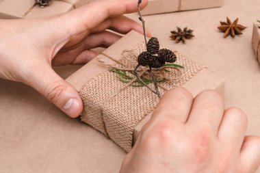 Eko-stil hediyelerin Noel süslemesi, erkek eli yakın çekim. Hediye kutuları el sanatları kağıdına sarılmış, thuja yaprakları ve koni ile süslenmiş. Noel, yeni yıl ve çevre dostu konsept..