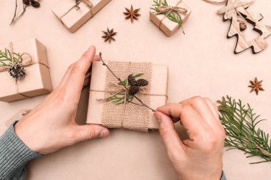 Hediyelerin eko-stil dekorasyonu, erkek eli yakın çekim, üst görünüm. Hediye kutuları el sanatları kağıdına sarılmış, thuja yaprakları ve koni ile süslenmiş. Noel, yeni yıl ve çevre dostu kavram..
