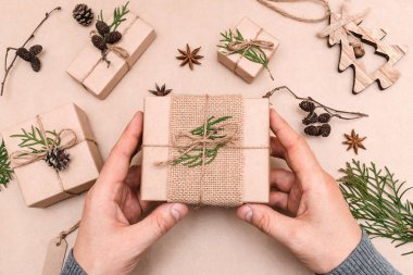 Hediyelerin eko-stil dekorasyonu, erkek eli yakın çekim, üst görünüm. Hediye kutuları el sanatları kağıdına sarılmış, thuja yaprakları ve koni ile süslenmiş. Noel, yeni yıl ve çevre dostu kavram..
