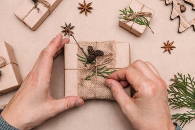 Hediyelerin eko-stil dekorasyonu, erkek eli yakın çekim, üst görünüm. Hediye kutuları el sanatları kağıdına sarılmış, thuja yaprakları ve koni ile süslenmiş. Noel, yeni yıl ve çevre dostu kavram..