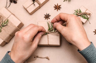 Hediyelerin eko-stil dekorasyonu, erkek eli yakın çekim, üst görünüm. Hediye kutuları el sanatları kağıdına sarılmış, thuja yaprakları ve koni ile süslenmiş. Noel, yeni yıl ve çevre dostu kavram..