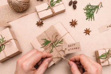 Hediyelerin eko-stil dekorasyonu, erkek eli yakın çekim, üst görünüm. Hediye kutuları el sanatları kağıdına sarılmış, thuja yaprakları ve koni ile süslenmiş. Noel, yeni yıl ve çevre dostu kavram..