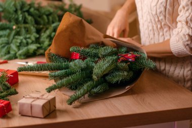 Evde köknar dallarından bir buket yapma süreci, kraft kağıdına sarma, kadının ellerine yakın çekim. Yeni yıl, Noel ve çevre dostu kavram. Seçici odaklanma..