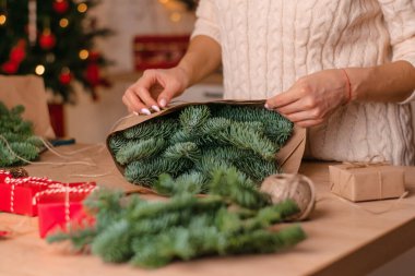 Evde köknar dallarından bir buket yapma süreci, kraft kağıdına sarma, kadının ellerine yakın çekim. Yeni yıl, Noel ve çevre dostu kavram. Seçici odaklanma..