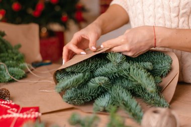 Evde köknar dallarından bir buket yapma süreci, kraft kağıdına sarma, kadının ellerine yakın çekim. Yeni yıl, Noel ve çevre dostu kavram. Seçici odaklanma..