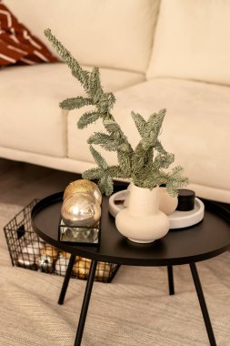 Şenlikli bir ev. Hafif bir kanepe, içinde vazo ve köknar dalları olan bir masa. Masadaki Noel süsleri. Yeni yıl ve Noel kavramı. Seçmeli odaklanma..