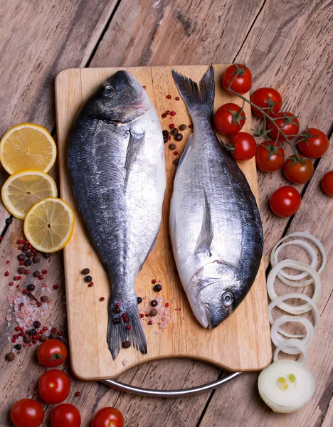 Two fresh gilt-head bream fish on cutting board with lemon,onion and cherry tomato — Stock Photo, Image