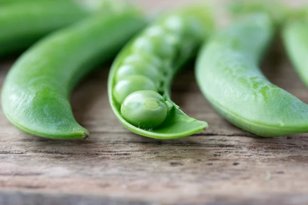 Pods of green peas on old wooden desk — Stock Photo, Image