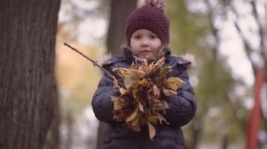 Ceketli ve şapkalı bulanık küçük kız havaya yapraklar fırlatıyor. Sonbahar konsepti.