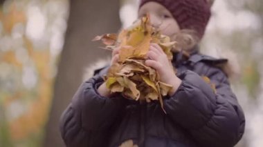 Ceketli ve şapkalı bulanık küçük kız havaya yapraklar fırlatıyor. Sonbahar konsepti.