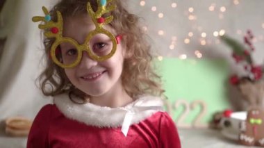 Bulanık kıvırcık kız Noel gözlüğü takıyor, kameraya bakıyor ve gülümsüyor. Noel tatili çocukluk konsepti. Noel 'in tadını çıkarıyorum.