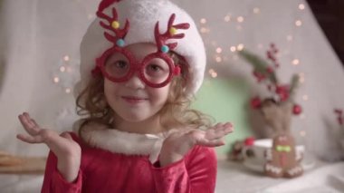 Noel Baba şapkalı bulanık küçük kız Noel gözlüğü takıyor, kameraya bakıyor ve gülümsüyor. Xmas çocukluk tatili konseptini sunar. Noel 'in tadını çıkarıyorum.