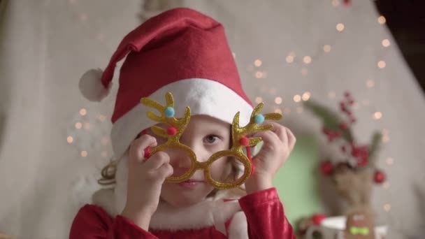 Zamazana Dziewczynka Czapce Mikołaja Zakładająca Świąteczne Okulary Patrząca Kamerę Uśmiechnięta — Wideo stockowe