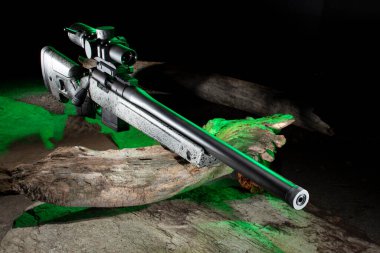 Green side lighting on a bolt action rifle and scope with a log on rocks
