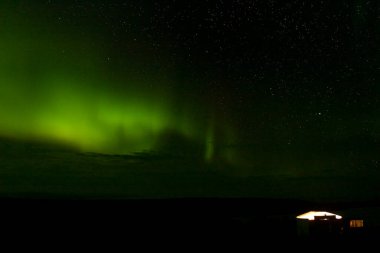 Hunting shack lit up with the Northern lights and stars above