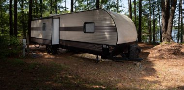 Camping trailer in a shady spot with Jordan Lake in the distance.