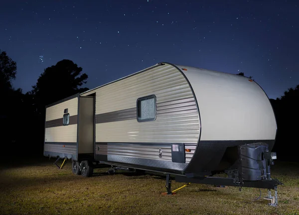 Travel trailer on a grassy field with bright stars above at night
