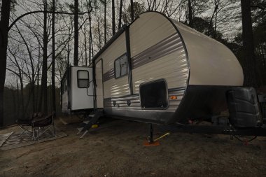 Gün batımından sonra kamp alanı önünde bir karavan ve sandalyelerle.