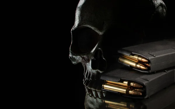 High capacity AR-15 magazines loaded with ammunition and a skull behind on a black background.