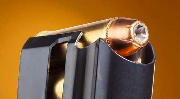 Close up view of a hollow point bullet in a pistol magazine with orange background