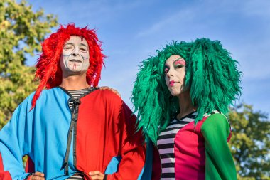 Parkta birbirine bakan renkli kostümlü mutlu palyaçolar.