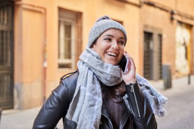 Dış giyimli bir kadın cep telefonundan konuşuyor.