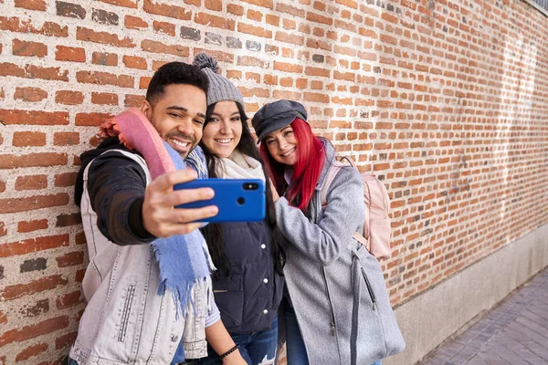 Sonriendo amigos multiétnicos tomando selfie en el teléfono inteligente cerca de la pared de ladrillo — Foto de Stock