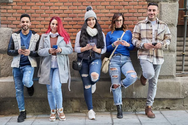 Diversos amigos con teléfonos inteligentes apoyados en la pared de ladrillo — Foto de Stock