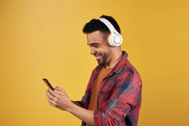 Kulaklık takmış, akıllı telefonları karıştıran içerik sahibi etnik adam.