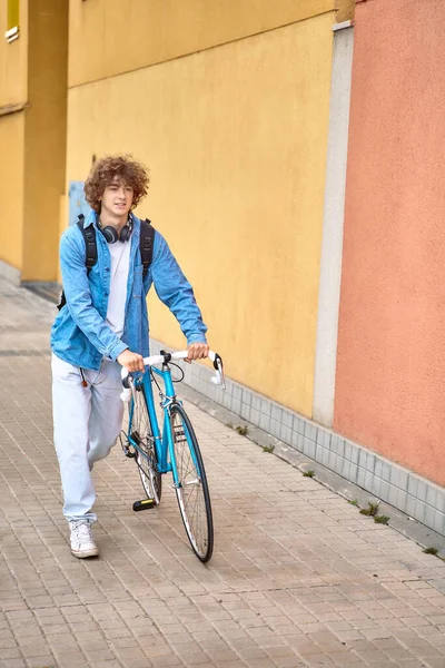 Siswa berambut keriting muda dengan headphone berjalan ke universitas dengan sepeda — Stok Foto