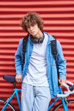 Gülümseyen adam bisiklete yaslanıyor ve kırmızı duvarda tırtıklı.
