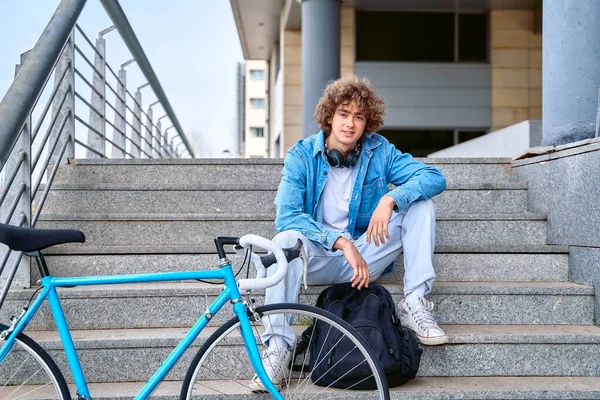 Pria tersenyum dengan ransel duduk di tangga dekat sepeda — Stok Foto