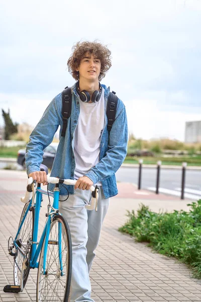 Siswa berambut keriting muda dengan headphone berjalan ke universitas dengan sepeda — Stok Foto