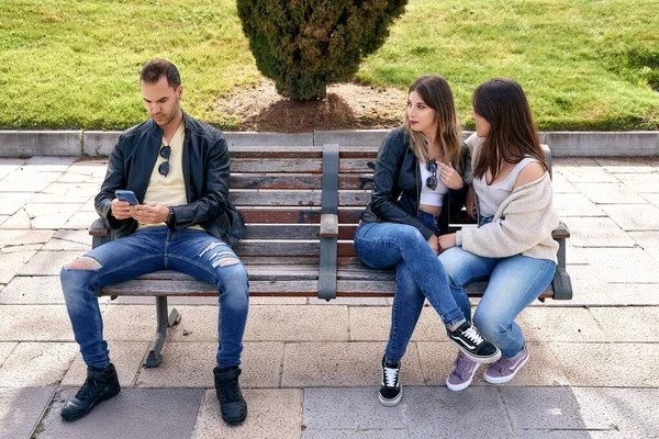 Two friends sitting on a bench next to an unknown boy. — ストック写真