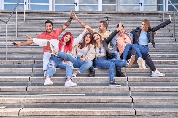 Estudiantes multirraciales alegres sentados en las escaleras y levantando brazos en la calle — Foto de Stock