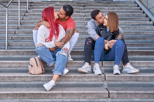 屋外の階段で一緒に座って時間を楽しんでいる間に2人の若いカップルがキスと抱擁 関係と愛の概念 — ストック写真