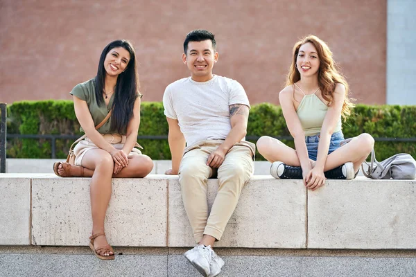 屋外で一緒に座っている間にカメラを見て笑顔の多人種の友人 友情の概念 — ストック写真