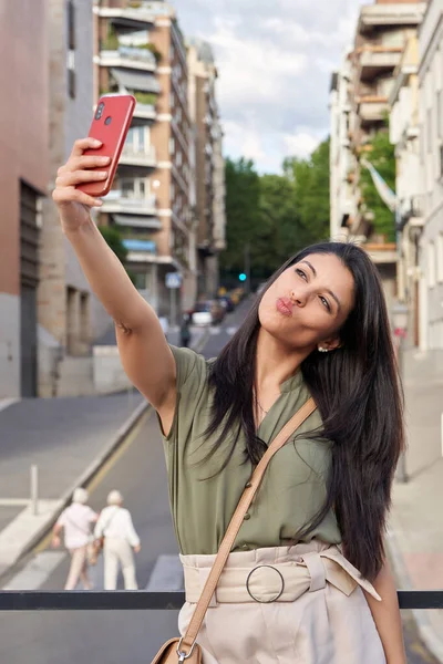 Confident woman taking a selfie with a mobile phone outdoors on city street. Technology and urban lifestyle concept.