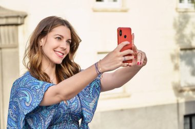 Gülümseyen kadın sokakta cep telefonuyla selfie çekiyor. Teknoloji, sosyal medya ve şehir yaşam tarzı kavramı.