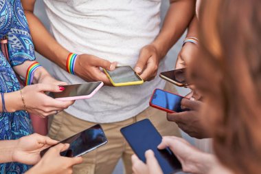 LGBT gökkuşağı bayraklı bir grup çok ırklı insan cep telefonlarını yan yana dururken kullanıyor. Çeşitlilik, LGBT, birlik ve teknoloji kavramı.