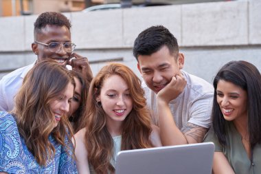 Dışarıdaki merdivenlerde dizüstü bilgisayardan bir şey izlerken gülümseyen çok ırklı bir grup insan. Kentsel yaşam tarzı, teknoloji ve takım konsepti.