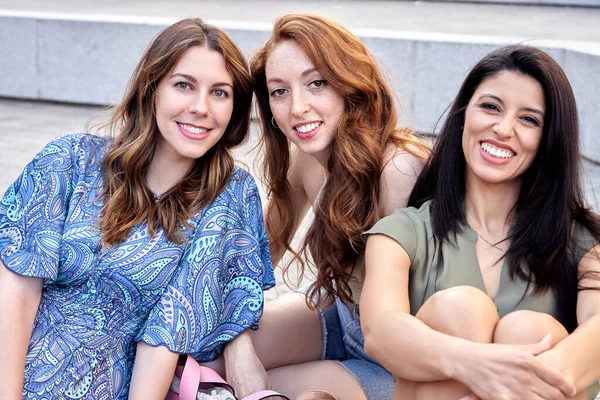 屋外に座っている間にカメラを見て笑顔の3人の女性の友人 友情の概念 — ストック写真