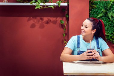 Woman looking away and smiling while drinking a smoothie sitting at a coffee shop. Healthy lifestyle and drinks concept.