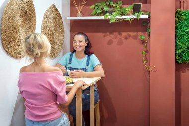 Two female friends talking while having breakfast together in a coffee shop. Friendship and food concept.