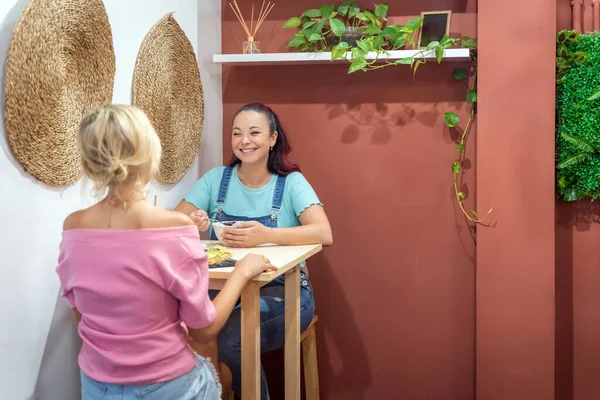 Two female friends talking while having breakfast together in a coffee shop. Friendship and food concept.